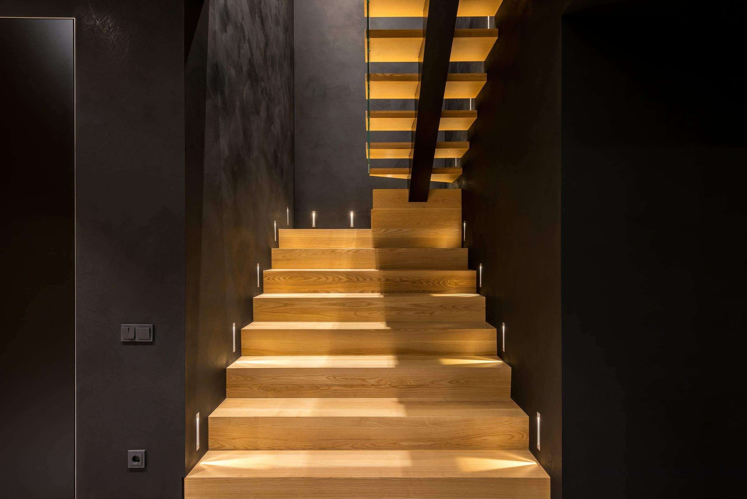 Escalier en chêne aux marches éclairées, entre deux murs sombres